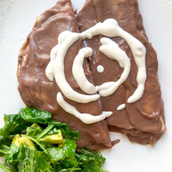 Las enfrijoladas son uno de esos platillos que siempre le pido a mi suegra cuando los visitamos. Tan simples y tan deliciosas, pero ¡ay!, qué pesadas pueden llegar a ser. Los frijoles refritos, muchas veces cocinados el día anterior y luego fritos en manteca, pueden hacer la digestión mucho más lenta y pesada. En México lo saben bien, y en el mundo árabe hasta existe una broma: cuando alguien está lento o sin energía para hacer sus cosas, se le pregunta si comió frijoles pesados en la mañana. Porque eso hacen: generan pesadez en el cuerpo y en la mente. Esta versión es una alternativa más balanceada: sigue siendo sabrosa, reconfortante y hogareña, pero sin esa carga digestiva que a veces acompaña la versión tradicional. Los frijoles se cocinan con especias que los hacen más ligeros, y el relleno de verduras salteadas aporta frescura y ligereza, manteniendo todo el placer de unas enfrijoladas, pero con una sensación mucho más nutritiva y estable. Es ideal para el otoño y el inicio del invierno, cuando el cuerpo agradece comidas más densas pero equilibradas que combinan saciedad con calor.