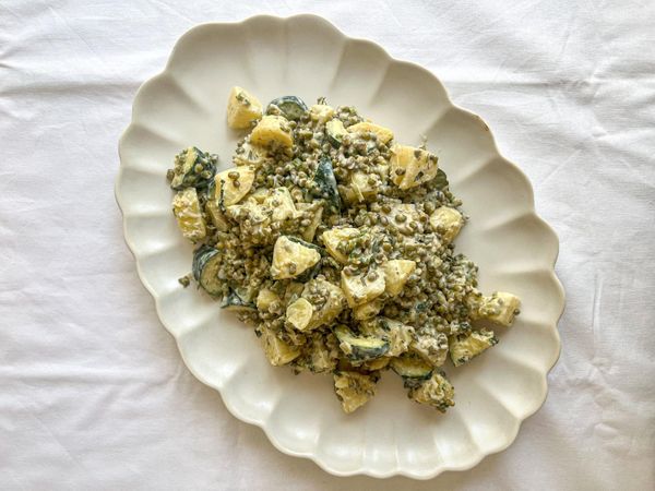 El frijol mung es una de las legumbres más ligeras y digestivas en Ayurveda, especialmente recomendado para quienes buscan proteína vegetal sin pesadez ni inflamación. En esta ensalada se combina con papas suaves y dulces (o calabacín, en caso de enfermedad autoinmune), equilibradas con el frescor del apio y especias digestivas como el cardamomo, el comino y el cilantro en polvo. En nuestros recetarios no verás tantas recetas con papa, ya que en exceso puede resultar pesada, aumentar la mucosidad y ralentizar la digestión. Sin embargo, también creemos en la flexibilidad: cuando se prepara con las especias correctas y en cantidades equilibradas, la papa puede ser nutritiva y satisfactoria. Esta receta es un buen ejemplo de cómo disfrutarla de manera ligera y en balance. El aderezo cremoso de tahini, limón y eneldo (o albahaca) aporta untuosidad, minerales y un sabor refrescante que armoniza todo el plato. Esta preparación da estabilidad, frescura y energía sostenida sin sobrecargar la digestión. Es ideal para la primavera y el verano, cuando el cuerpo agradece comidas ligeras, pero también puede disfrutarse en días frescos como ensalada tibia. Puede servirse en la comida como plato principal, acompañado de granos como quinoa, pasta de quinoa o arroz.