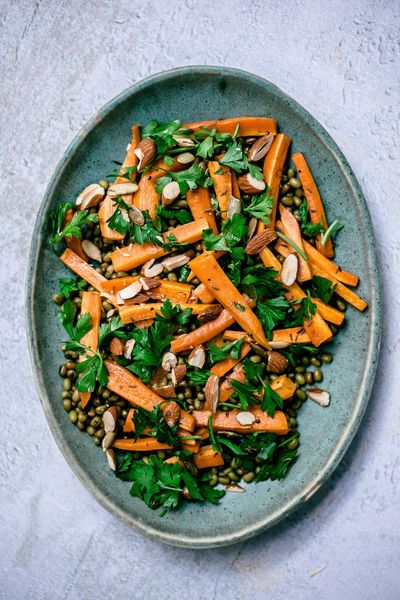 Cuando pensamos en ensaladas, solemos imaginar lechuga cruda y verduras frías, que muchas veces resultan pesadas y difíciles de digerir. En Ayurveda, las ensaladas no tienen que ser así: se pueden preparar tibias, con ingredientes cocidos y especias que favorezcan la digestión. Esta ensalada de zanahorias horneadas con frijol mungo cocido es un ejemplo perfecto: ligera, aromática y llena de sabor gracias al hinojo, comino, hierbas frescas y cítricos. El resultado es una ensalada nutritiva, equilibrada y digestiva que se disfruta con facilidad en cualquier época del año. En primavera y verano su frescura cítrica resulta revitalizante, mientras que en otoño e invierno las zanahorias horneadas le dan un carácter cálido y reconfortante. Se puede acompañar con algún grano como quinoa, o incluso probarla con couscous y espinaca salteada para convertirla en una comida completa; o disfrutarla tal como es para la cena. Solo recuerda no excederte con la cantidad de frijoles, ya que en exceso pueden causar indigestión.