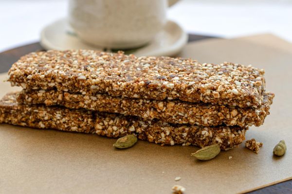 Un snack nutritivo, energético y medicinal con una larga tradición en Ayurveda y en muchas cocinas del sur de Asia. Estas trufas o barritas combinan frutos secos, semillas, dátiles y especias aromáticas que no solo aportan energía estable, sino que también fortalecen el cuerpo y equilibran el sistema digestivo. Este tipo de preparación es conocido en India como laddoo, y suele darse en contextos muy específicos: a quienes se sienten débiles o han perdido peso, a mujeres embarazadas (con menor cantidad de canela y nuez moscada), a madres lactantes como snack que apoya la producción de leche y la recuperación, e incluso a niños mayores de un año como alternativa nutritiva y natural a los dulces procesados. En esta versión hemos sustituido parte de las nueces por granos inflados (cebada, amaranto o quinoa), lo que hace la preparación un poco más ligera sin perder la saciedad y el carácter fortalecedor. Los dátiles aportan dulzor natural y minerales; las almendras, nueces y semillas de calabaza suman grasas saludables y proteínas vegetales; y las especias, canela, cardamomo y nuez moscada, no solo aromatizan, sino que también estimulan suavemente la digestión y hacen que el snack no resulte pesado. Se pueden presentar en forma de trufas o barras, y disfrutarse como parte del desayuno (acompañadas de leche tibia para mayor nutrición) o como snack energético a lo largo del día. Es ideal en otoño e invierno, cuando el cuerpo agradece bocados nutritivos, untuosos y especiados que brindan sostén y calor. Es un snack ideal de recuperación para personas con debilidad o desgaste.