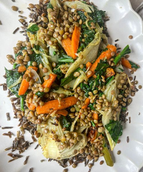 Un plato nutritivo, cálido y lleno de sabor que combina la suavidad de las lentejas con el arroz salvaje y el dulzor natural de las zanahorias. El arroz salvaje es en realidad una semilla acuática, destaca por su alto contenido en antioxidantes y minerales, y aporta una textura firme y saciante sin resultar pesado.
El hinojo, tanto en semillas como en bulbo, aporta un toque aromático y digestivo que equilibra la preparación, mientras que las hojas verdes (kale o espinaca) añaden frescura y minerales. El toque final de ralladura y jugo de limón no solo ilumina el sabor, sino que también ayuda a que el hierro presente en las lentejas y las espinacas se vuelva “más biodisponible”, favoreciendo su absorción.
El uso de ghee y especias suaves como canela y tomillo convierte este plato en una comida completa, ligera y profundamente satisfactoria. Es perfecto para los días en los que se busca sostén sin pesadez, ideal como plato principal vegetariano completo. Es ideal en otoño, invierno y primavera, cuando el cuerpo agradece preparaciones tibias, especiadas y con el equilibrio justo entre dulzor, frescura y sustento.
