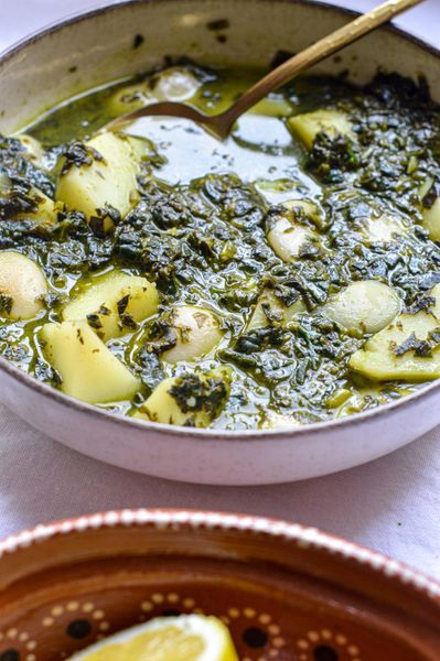 Este es un platillo muy querido en la cocina de los judíos de Túnez, profundamente herbolario, reconfortante y lleno de sabor. Siempre que lo preparo me recuerda a un plato de Jordania llamado "mlokhieh" (jew’s mallow), verde, aromático y muy nutritivo. Son de esas recetas donde las hierbas no son un adorno, sino la base del plato. El cilantro, el perejil y la espinaca aportan una gran cantidad de minerales, clorofila y frescura. En Ayurveda, las hierbas verdes se valoran mucho por su capacidad de nutrir sin pesadez y apoyar procesos de depuración suave del cuerpo. Al mismo tiempo, el plato es muy satisfactorio porque combina frijoles y papas, dando estabilidad y energía sostenida. Si lo deseas, puedes sustituir los frijoles blancos por pollo, aunque en esta receta las legumbres quedan especialmente deliciosas y le dan ese carácter tradicional. También puedes cambiar las papas por zanahorias si estás manejando temas de inflamación o buscas una opción más ligera. Como habrás notado, en mis recetas casi no uso ajo ni cebolla. Pero aquí un toque de ajo realmente vale la pena: ayuda a encender el fuego digestivo y aporta profundidad de sabor. La receta original probablemente llevaría mucho más ajo, pero no hace falta; una pequeña cantidad cumple su función sin abrumar. La asafétida es opcional pero muy recomendable, especialmente cuando hay legumbres, ya que ayuda a hacerlas más fáciles de digerir y a reducir gases. Servido con arroz al lado, se convierte en una comida completa, cálida y muy satisfactoria: de esas que nutren, reconfortan y se sienten vivas.