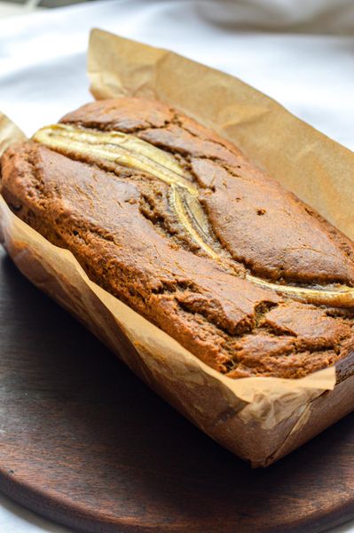 El pan de plátano es uno de esos clásicos de cocina casera que casi todos hemos probado alguna vez. Es muy común que las mamás lo preparen para sus hijos cuando los plátanos ya están demasiado maduros y nadie quiere comérselos. Pero cuando se prepara con ingredientes más integrales y con las especias adecuadas, puede convertirse en algo más que un simple postre: un alimento reconfortante que también cuida la digestión. El plátano maduro aporta dulzor natural, humedad y una energía nutritiva y estable. En Ayurveda se considera un alimento que nutre los tejidos y aporta sensación de satisfacción, especialmente cuando se combina con grasas buenas y especias digestivas. Las especias que usamos aquí, canela, cardamomo, anís, hinojo y clavo, no están solo por sabor. Su función es ayudar a que el cuerpo procese mejor la dulzura del plátano y de la harina, manteniendo el fuego digestivo activo para que el pan no se sienta pesado. Las especias cálidas son una forma tradicional de hacer que los postres y panes sean más fáciles de digerir. La linaza y la harina integral aportan estructura y fibra, mientras que el aceite de oliva mantiene el pan húmedo y suave. El plátano colocado encima antes de hornear se carameliza ligeramente y le da una textura y aroma muy especial. Es un pan perfecto para otoño, invierno y comienzos de primavera, cuando el cuerpo suele tolerar mejor preparaciones horneadas y especiadas. Funciona muy bien para un desayuno tranquilo o una merienda acompañada de una bebida caliente. Un pan sencillo, aromático y profundamente reconfortante.