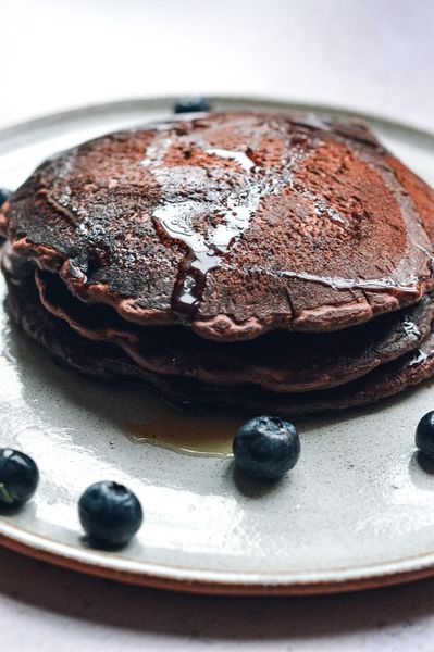 A estas alturas ya saben que en casa somos fans de los pancakes. Tener un hijo pequeño te invita a reinventar recetas constantemente y esta es una de esas versiones que nació de una necesidad muy concreta: pocas horas de sueño y un antojo fuerte de algo chocolatoso y reconfortante. El cacao no es el alimento más típico de la primavera, pero hay momentos en que el cuerpo pide algo que ancle, que sostenga. Estas semanas de destete nocturno han sido eso y estos pancakes han cumplido exactamente esa función. La espelta los hace más digestivos que la harina de trigo convencional, el yogur y el jugo de limón activan el bicarbonato y los dejan increíblemente esponjosos. Son un desayuno para el fin de semana, para un momento en que quieres algo especial sin complicarte. En casa gustan mucho, y eso ya dice bastante. 