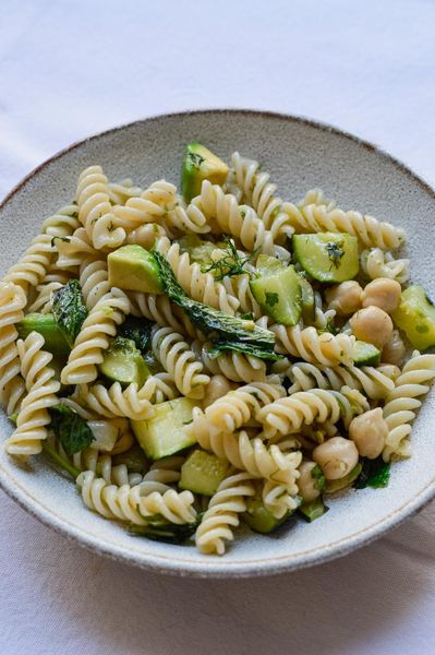 Este es el tipo de plato que hago cuando no tengo ganas de cocinar pero tampoco quiero comer cualquier cosa. Rápido, nutritivo y con muy poco que limpiar después, que no es un detalle menor. Un truco que uso seguido: la misma olla donde se cuece la pasta sirve de base para el cesto de vapor. Mientras el farro se cocina abajo, los espárragos y el calabacín se hacen arriba. Todo al mismo tiempo, todo en un solo lugar. Los espárragos son una de las verduras más interesantes de esta época. Aparecen en primavera por algo, tienen una cualidad naturalmente depurativa y ligera que encaja perfectamente con lo que el cuerpo está pidiendo en esta transición. El farro y los garbanzos tienen algo en común que los hace especialmente apropiados para la primavera: ambos son de los más secos dentro de su categoría. Esa cualidad más seca ayuda a equilibrar la humedad y la pesadez que tiende a acumularse durante el invierno. Si no encuentras pasta de farro, la de quinoa funciona muy bien como alternativa. La albahaca y la menta lo levantan, el eneldo tostado le da profundidad, y el limón y el aguacate al final lo redondean todo. Se sirve a temperatura ambiente, lo que también lo hace más fácil de digerir que un plato frío de nevera. Una comida completa sin ningún drama.