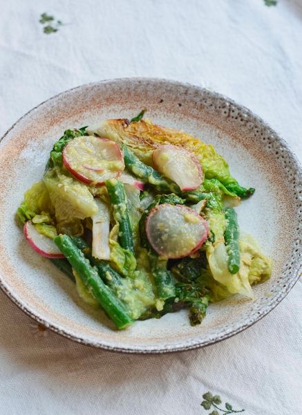 Una ensalada que no se siente como ensalada y eso es exactamente lo que la hace especial. Asar la lechuga y los rábanos en lugar de comerlos crudos cambia completamente la experiencia: los bordes dorados, la textura suave por dentro, el sabor más concentrado. Y desde una perspectiva digestiva también tiene más sentido, especialmente ahora que el calor está subiendo y el cuerpo pide cosas frescas pero no frías. Los ejotes son uno de esos ingredientes que cumplen doble función, aportan la parte de legumbre y al mismo tiempo actúan como verdura purificante, lo que las convierte en un elemento muy completo dentro del plato. Los rábanos también depuran, y la lechuga a la parrilla añade ligereza sin dejar de ser sustanciosa. El aderezo de aguacate es lo que une todo, cremoso, refrescante y con el jengibre justo para hacer que todo sea más fácil de digerir. El hinojo en polvo va en la misma línea. Cocinar las verduras, aunque sea brevemente, ya es un paso que el cuerpo agradece en comparación con una ensalada completamente cruda. Puedes servirla con quinoa para una comida completa, añadir una verdura que construye si necesitas más sustancia, o usarla como acompañamiento de pescado o carne a la plancha. Versátil, fresca y muy fácil de preparar.